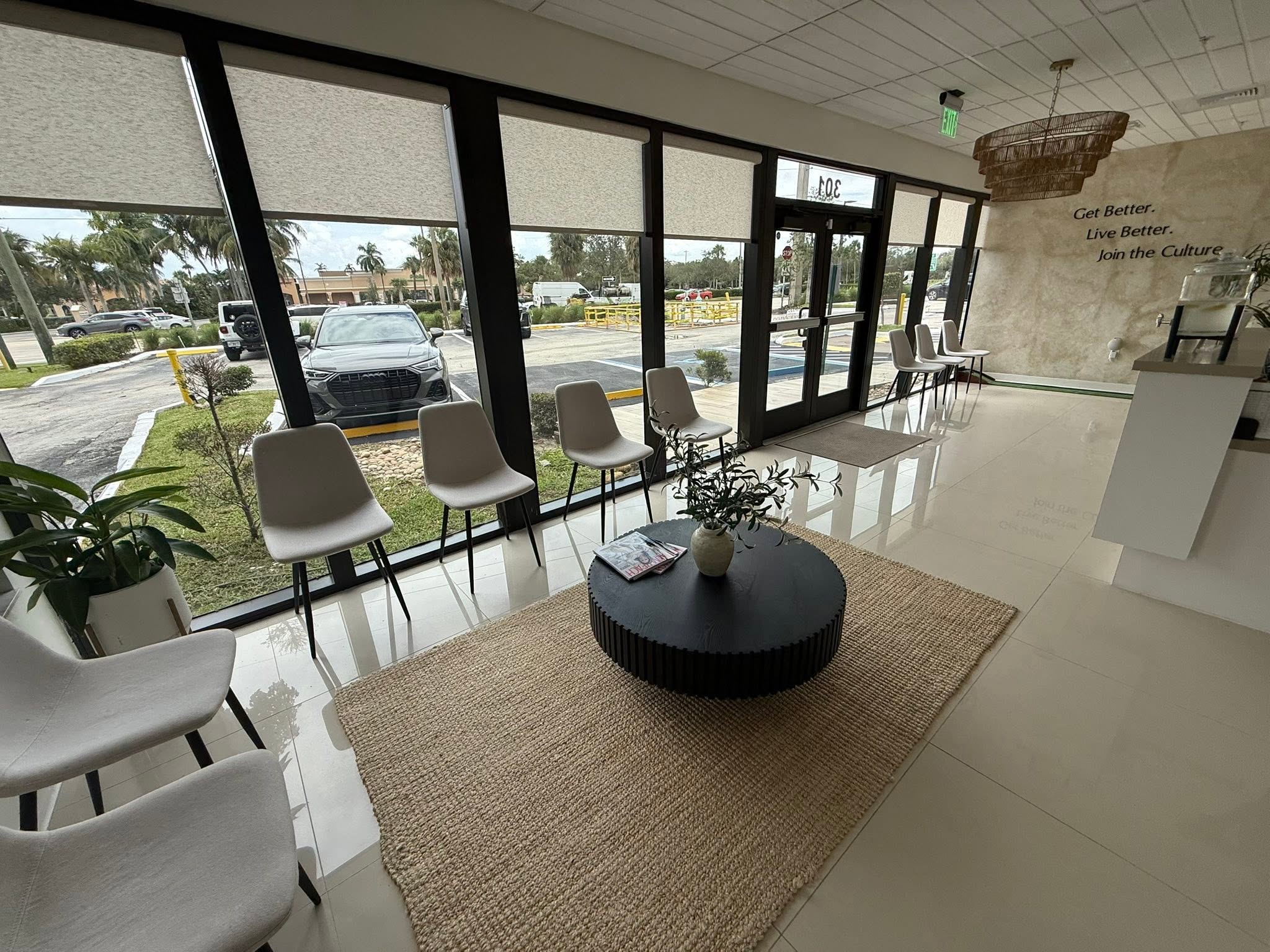 Modern medical office waiting room with white chairs, black round table, and large windows overlooking parking lot