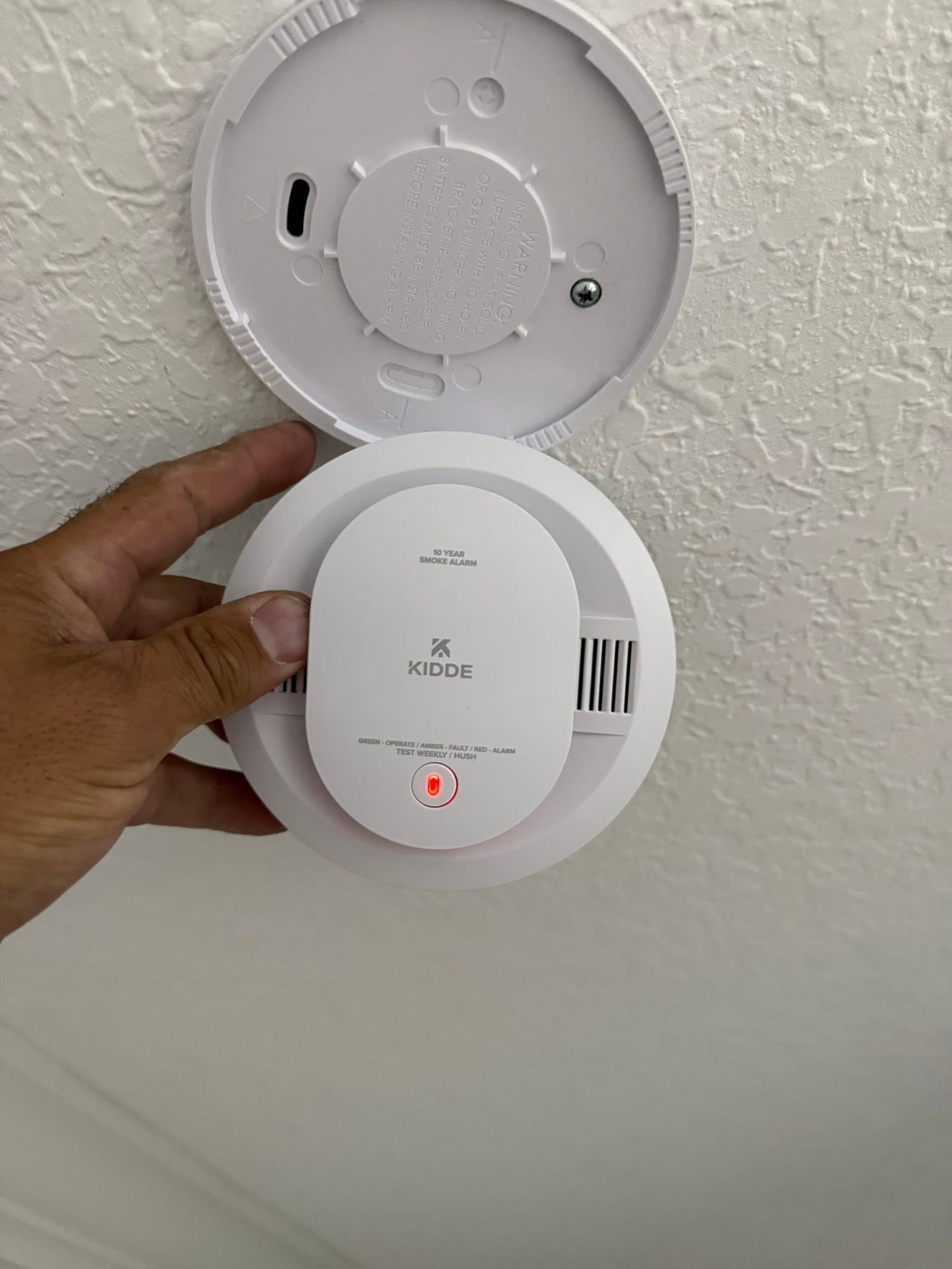 KIDDE smoke alarm being held in hand with mounting bracket visible above