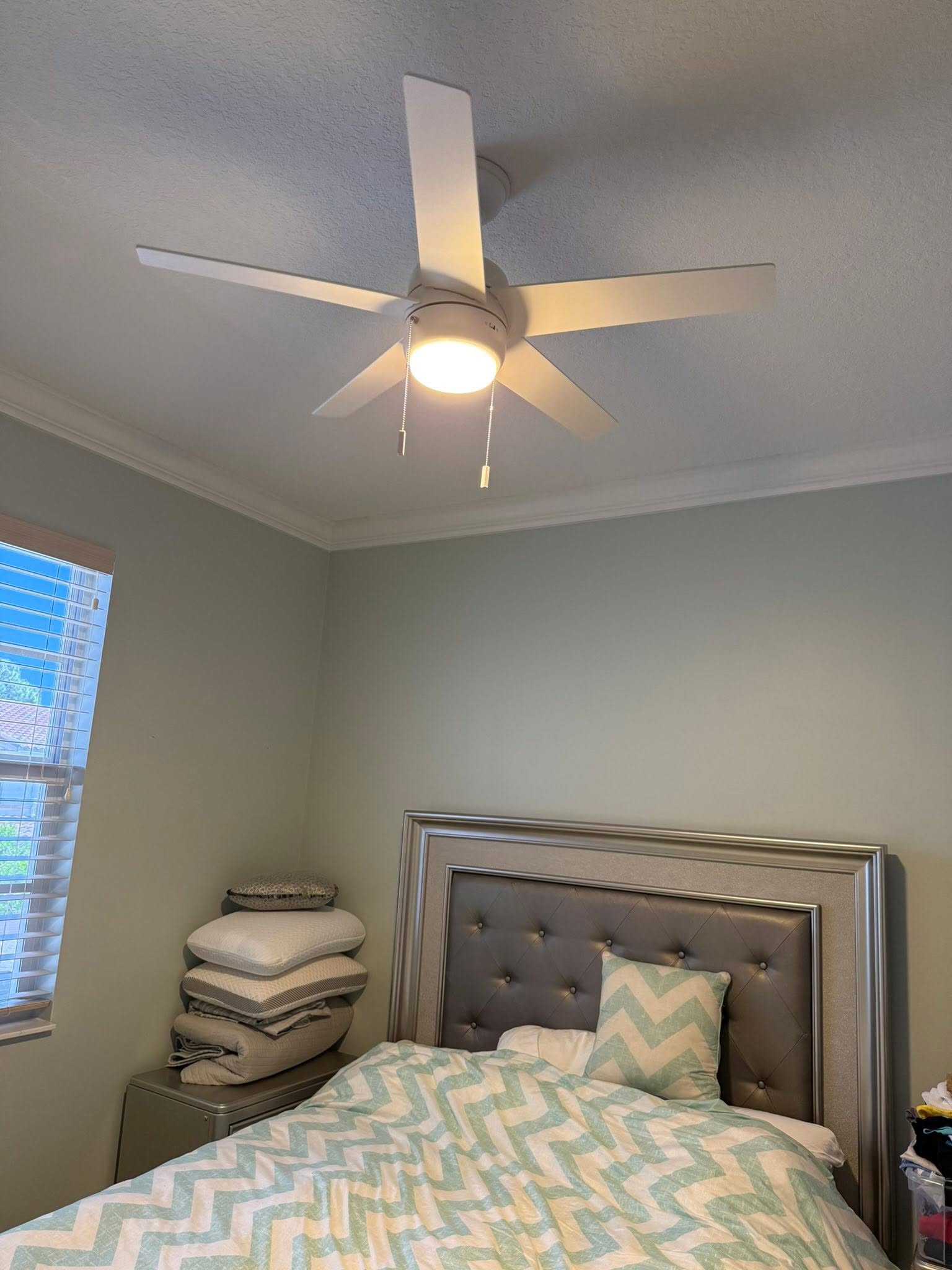 Ceiling fan with integrated light fixture in bright bedroom above bed