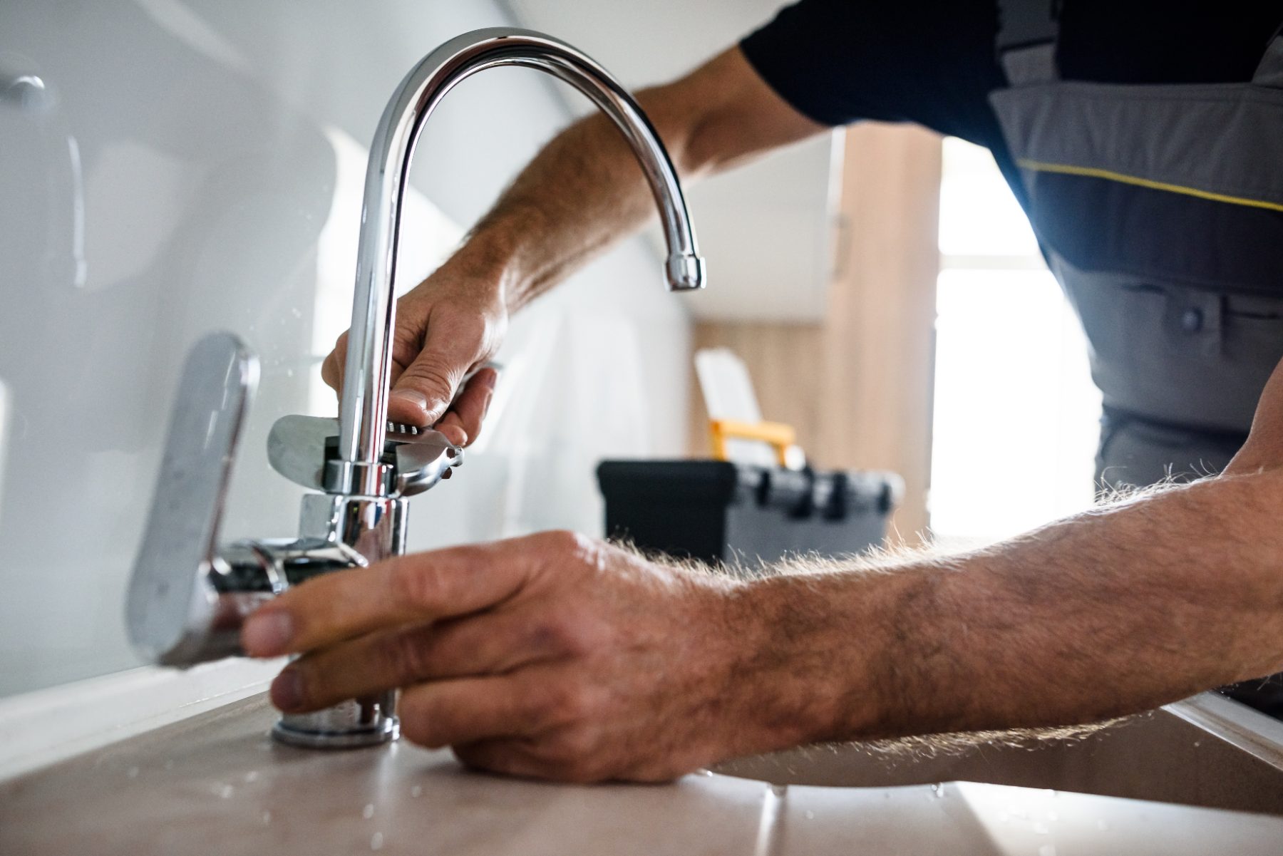 Plumber installing a modern chrome faucet on a white sink countertop