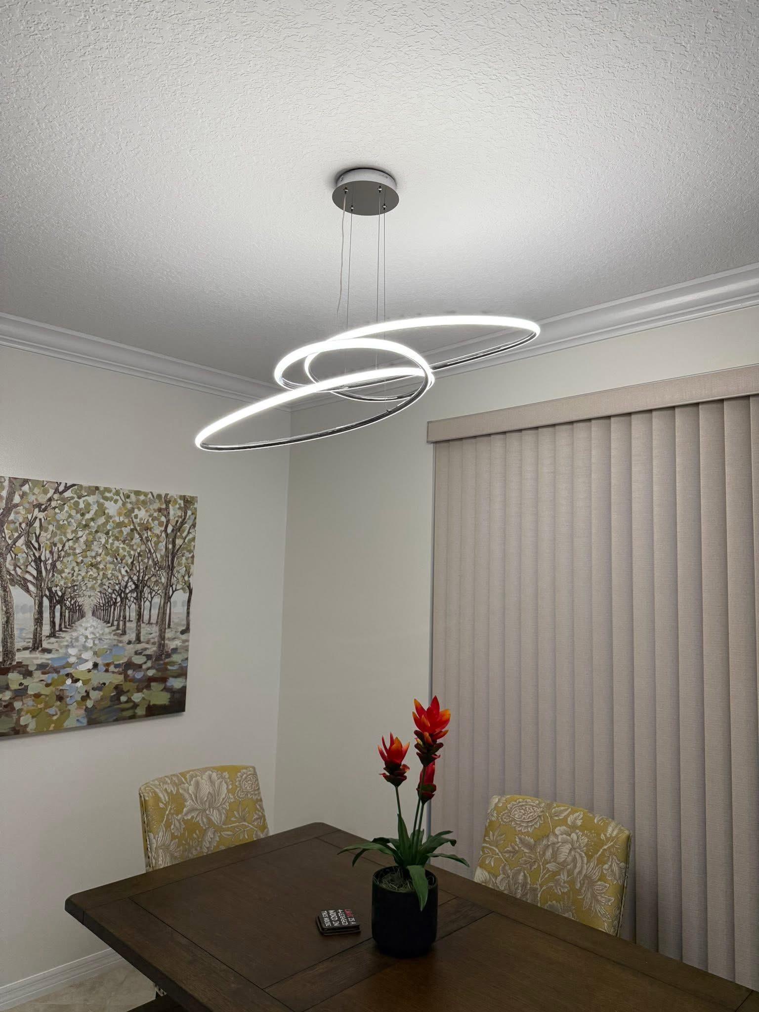 Modern spiral LED pendant light above dining table with chairs and red flowers