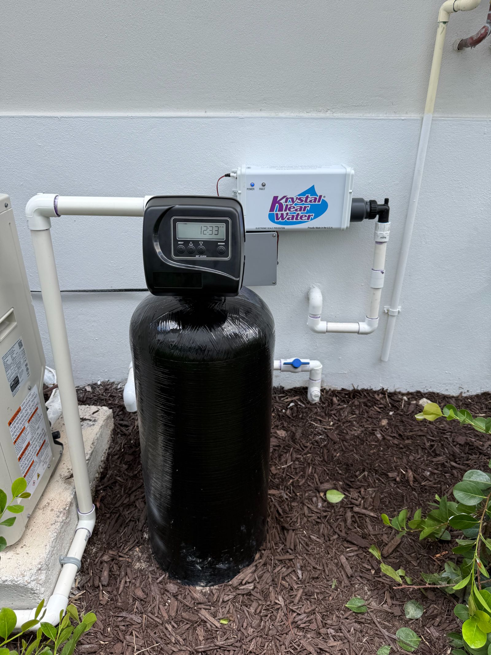 Water softener system with digital timer mounted on black resin tank against white wall